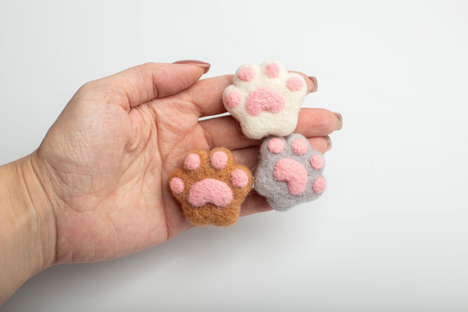 A soft brown, white and gray felt cat paw with pink pads for attached to a car air vent as a cute decorative clip or nature air freshener.
