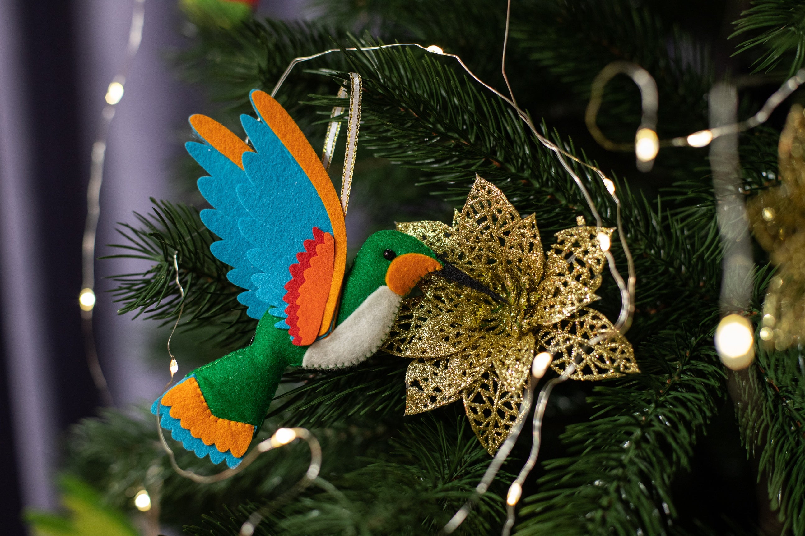 A handmade green felt hummingbird ornament with a white belly, blue wings, and a black beak