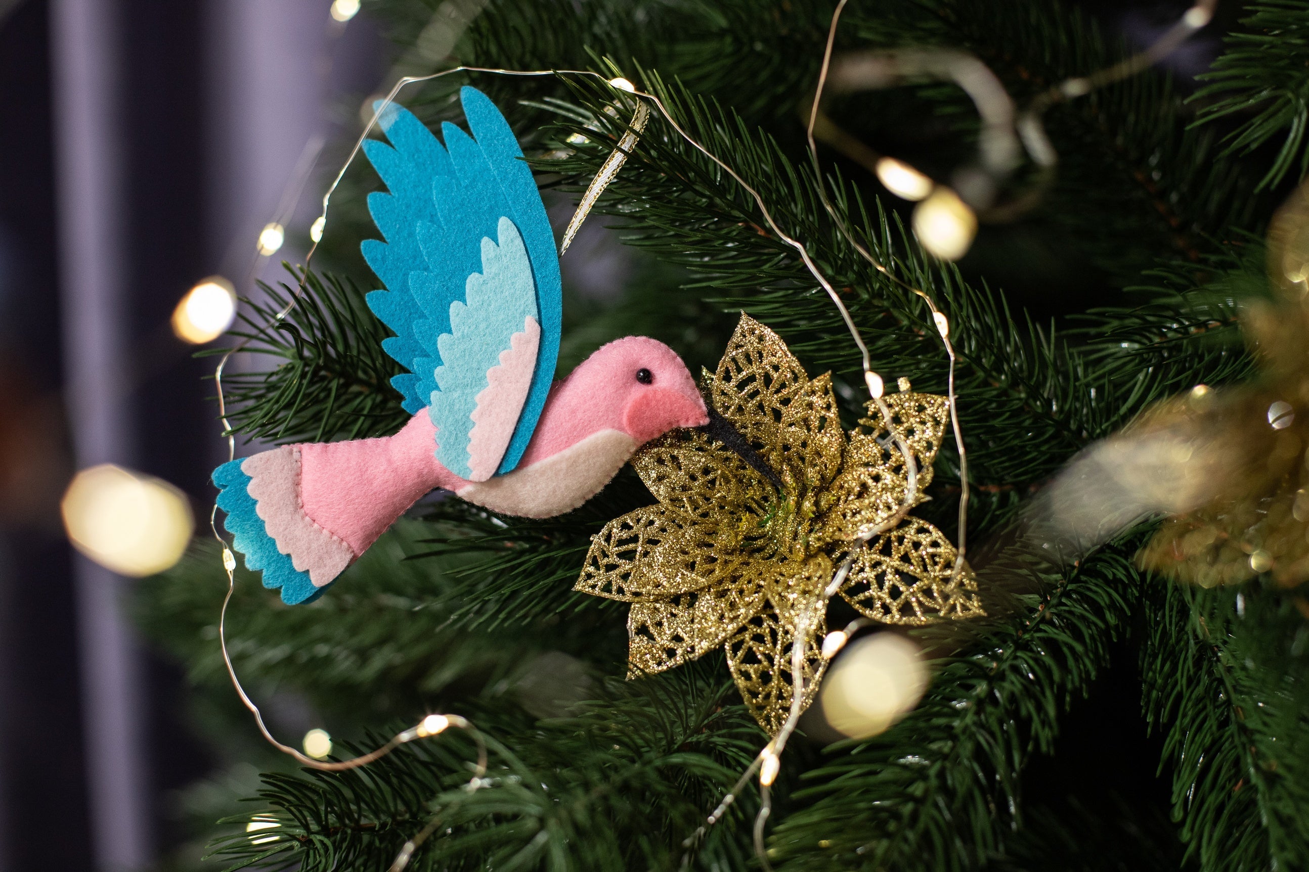 A handmade pink felt hummingbird ornament with a white belly, light blue wings, and a black beak